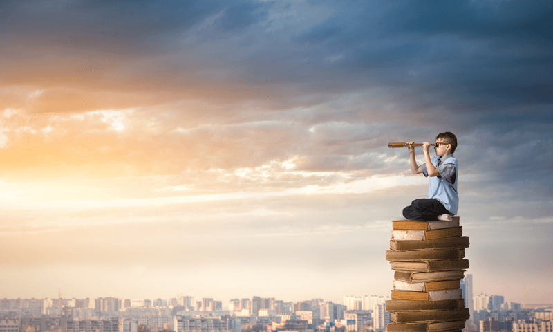 young kid looking through a telescope sitting on a pile of books